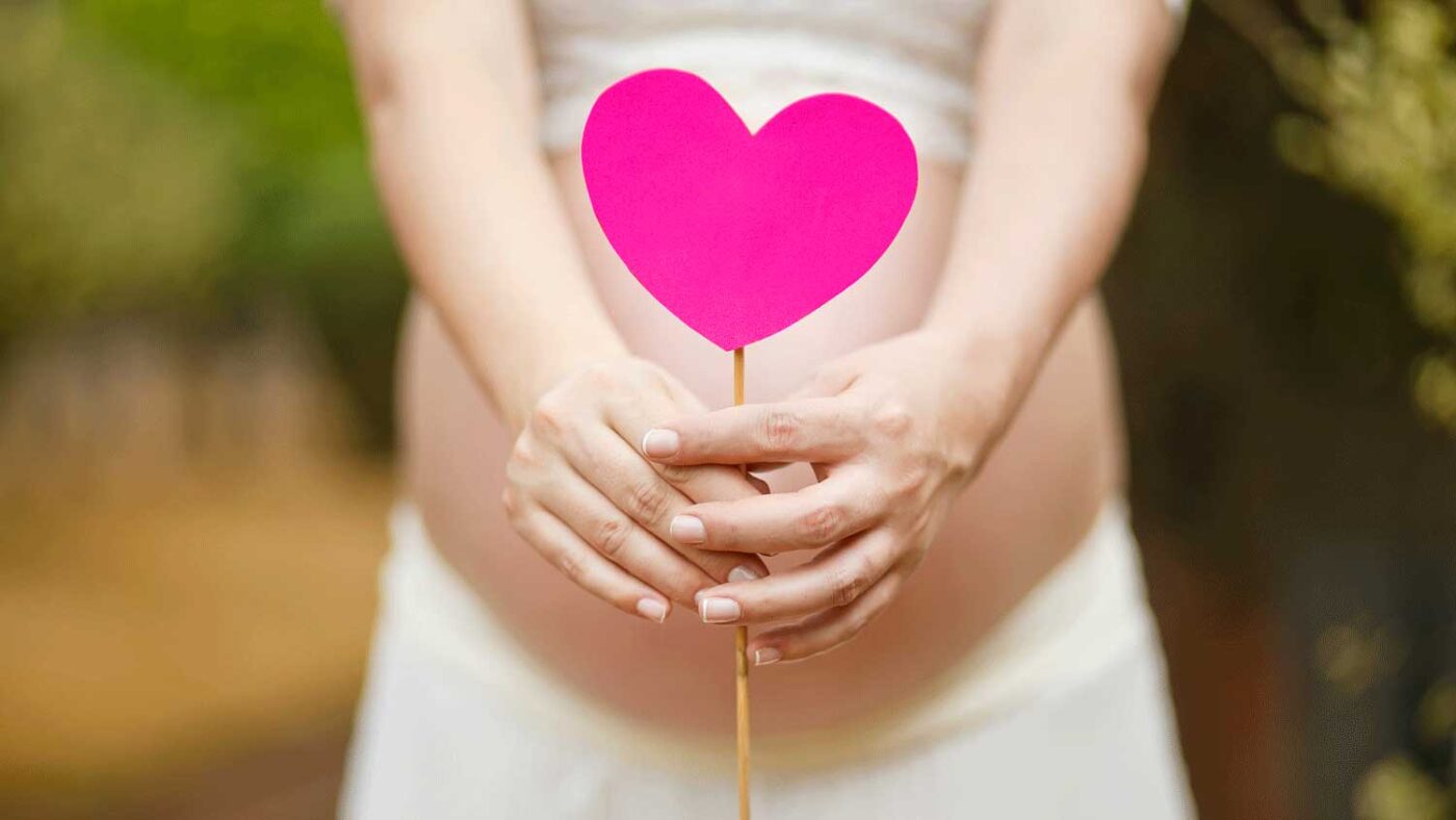 pregnant woman holding pink heart on a stick