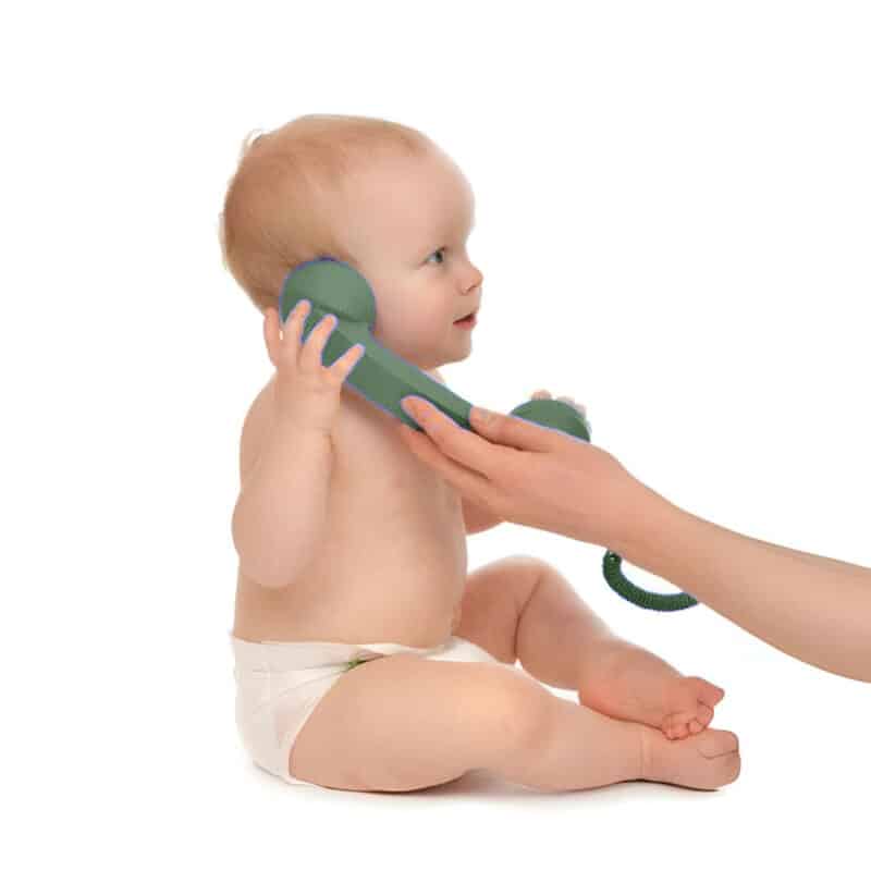 baby holding green old style phone to ear with mum's hand assisting